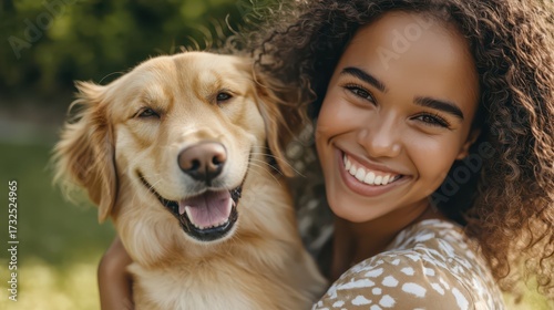 A joyful young woman smiles while holding her golden retriever, capturing a moment of happiness in a sunny outdoor setting.