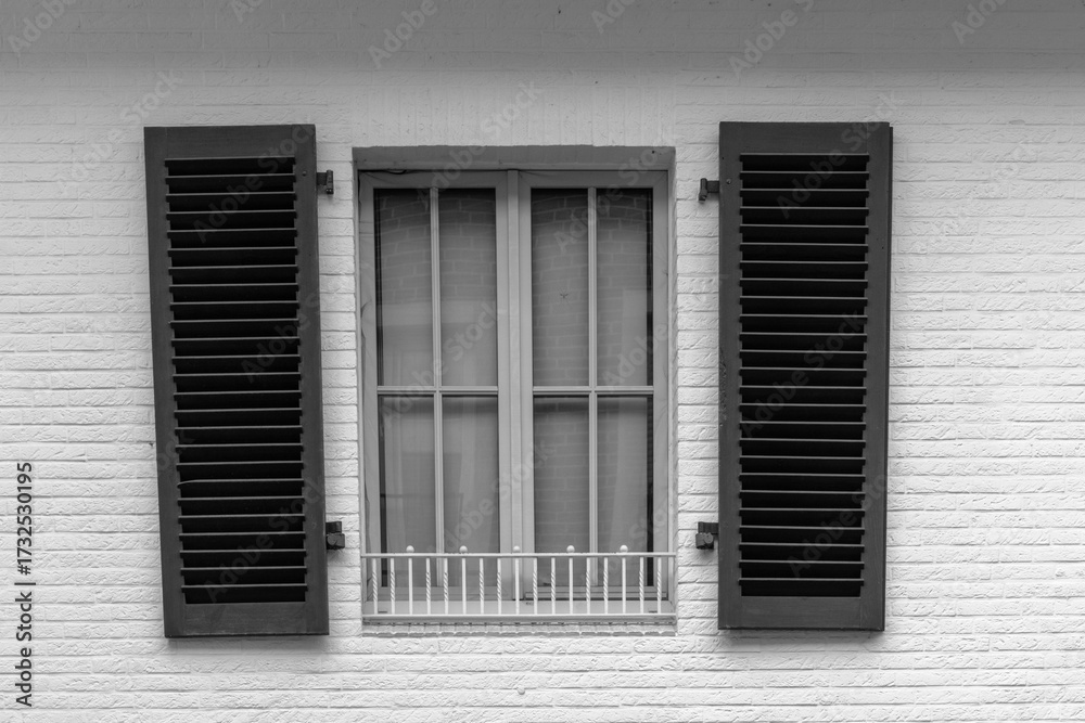 Fototapeta premium Shuttered window on a white brick wall with green shutters, highlighting architectural details in simple design