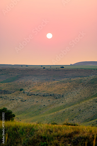 The sun sets over rolling steppe hills, painting the sky in soft orange hues.