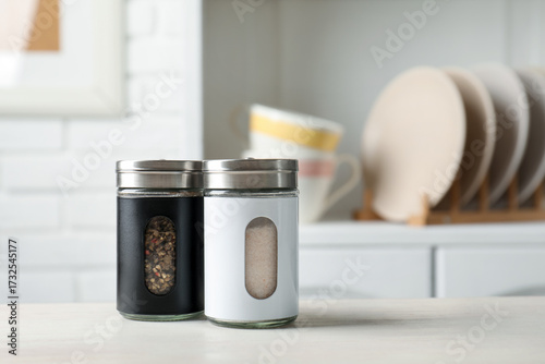 Salt and pepper shakers on light wooden table in kitchen, closeup. Space for text