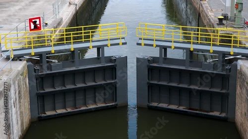 Water sluice lock gate on Main River Cargo vessel inland navigation in Wurzburg under cloudy sky. Historic town buildings and green riverside frame the modern waterway infrastructure