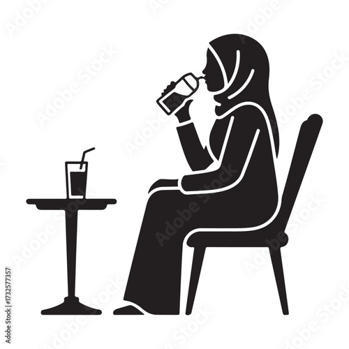 Woman wearing hijab drinking from a bottle while sitting at a table silhouette