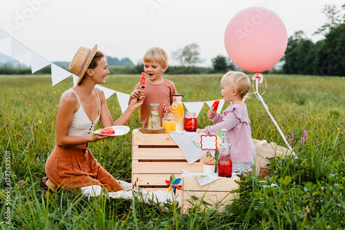 Foto Mother with little children having imaginary picnic in meadow