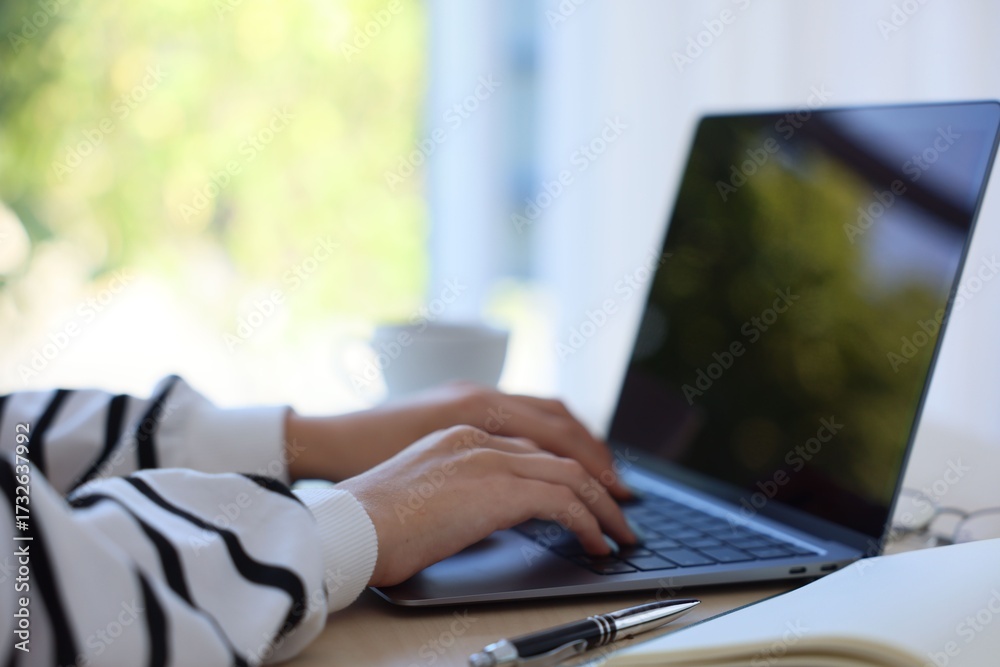 Fototapeta premium Woman working with laptop at table against blurred background, closeup