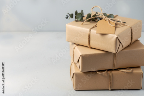Stack of three rustic gift boxes wrapped in natural kraft paper with twine, eucalyptus, and blank tag, banner with copy space.