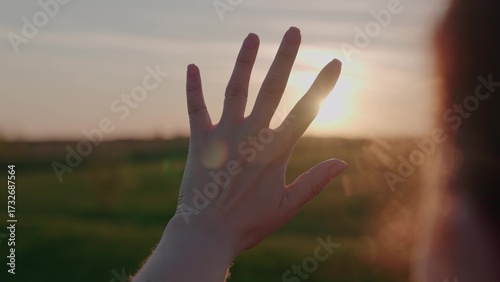 Fotografía Glare of the sun through the girl's fingers, woman dream of freedom, a man's journey at sunset, the bright light of sun on his hand, beautiful colored glare of dawn, praying without receiving energy