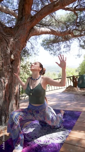 Woman practicing yoga pose outdoors on wooden deck under a tree	