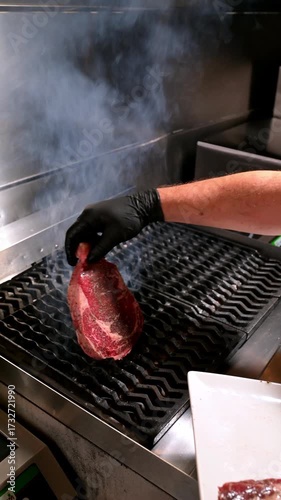 Chef places raw steak on a hot grill. Close-up of raw beef steak being placed on a hot grill by a chef wearing gloves.