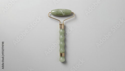 Minimalist flatlay of a single jade face roller with gold metal handle on a clean white and gray background, highlighting skincare, beauty tools, and self-care ritual.