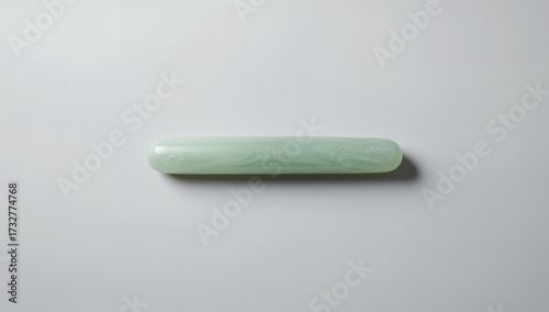 Minimalist flatlay of a single oblong jade stone with smooth, rounded edges on a clean, bright white background, emphasizing natural beauty, skincare wellness, and tranquil minimalism.