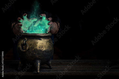 Witch's hands over a cauldron with a magic potion in a dark room. Witch casting spells on Halloween night
