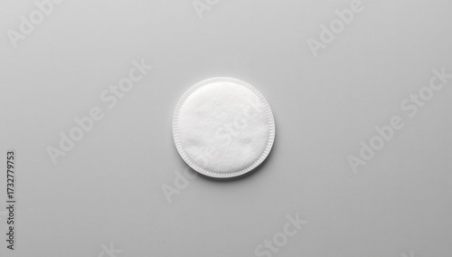 Minimalist overhead flatlay of a single, pristine white cotton pad or make-up removal disc centered on a clean light gray background, ideal for beauty, skincare, and medical themes.