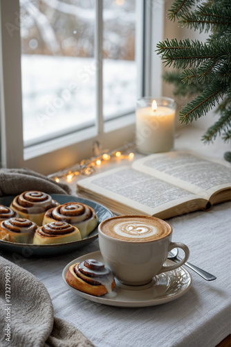 A cup of cappuccino with latte art sits on a small, decorated saucer beside a cinnamon rolls