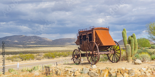 Foto Old stagecoach sits on a rocky outcrop overlooking a desert landscape under a cl