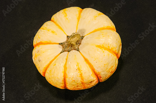 Top view, closeup of, a small, yellow and orange pumpkin with a black background, under strobe lighting