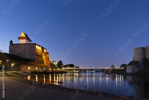 Narva Castle in Estonia illuminated at twilight with reflections in the Narva River, facing Ivangorod Fortress in Russia.