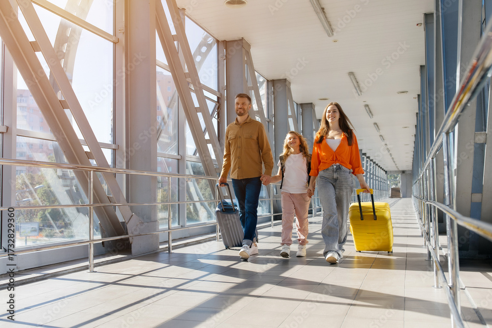 Fototapeta premium Happy european family walking side by side at airport with luggage suitcases, holding hands and smiling in sunlight, symbolizing cheerful bonding, lifestyle and holiday travel joy