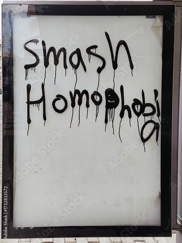A message painted on glass outdoors reads “smash homofobia” in black paint with drips.