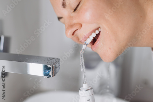 Close-up of a woman cleaning her teeth with a white portable water flosser. Concept: oral care and daily hygiene routine.