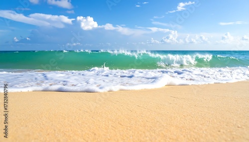 Fototapeta Naklejka Na Ścianę i Meble -  A tranquil beach scene features a vibrant turquoise wave crashing on the sun-kissed sand, with a bright blue sky and fluffy white clouds