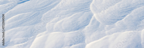 Beautiful winter background with snowy ground. Natural snow texture. Wind sculpted patterns on snow surface. Wide panoramic texture for background and design.
