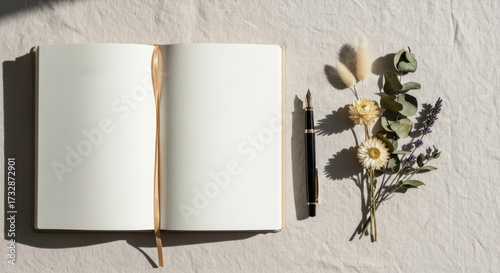Minimalist flat lay of an open blank notebook, elegant fountain pen, and dried flowers on a linen fabric. Creative writing, poetry, and mindfulness concept.