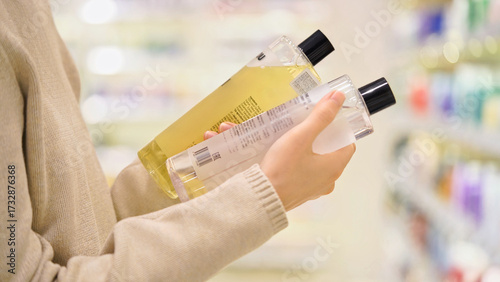 Konstfotografi Close up of woman comparing two shampoo bottles in a beauty store, reading labels and ingredients
