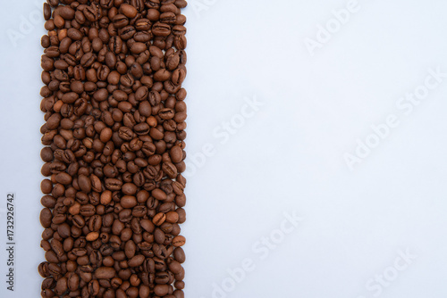 line of roasted coffee beans scattered on a white background