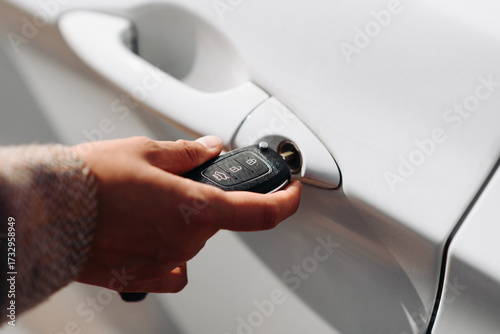 black car keys in woman hand, close-up view, white car in background, opening or closing car with signalization or alarm system, car theft, carjacking, car safety concept, selective focus
