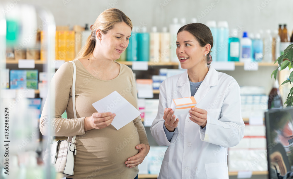 Obraz premium Young female pharmacist giving prescription pills to pregnant woman in pharmacy