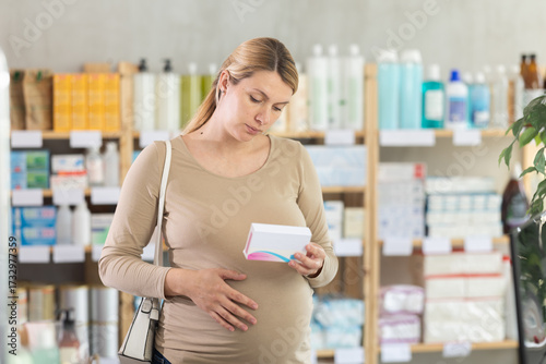 Obraz na płótnie Pregnant woman choose pills of iodide and folic acid in pharmacy, examine packaging