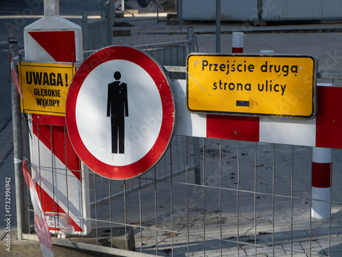 Zamknięte przejście dla pieszych oznaczone znakami zakazu i tablicami informacyjnymi podczas prac drogowych z ostrzeżeniem o głębokich wykopach