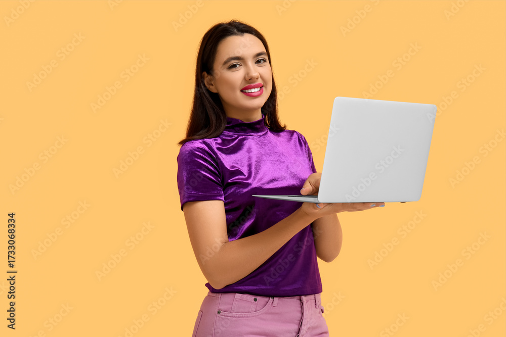 Naklejka premium Beautiful young happy woman with laptop on yellow background