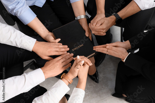 Business people praying with Holy Bible in office, top view