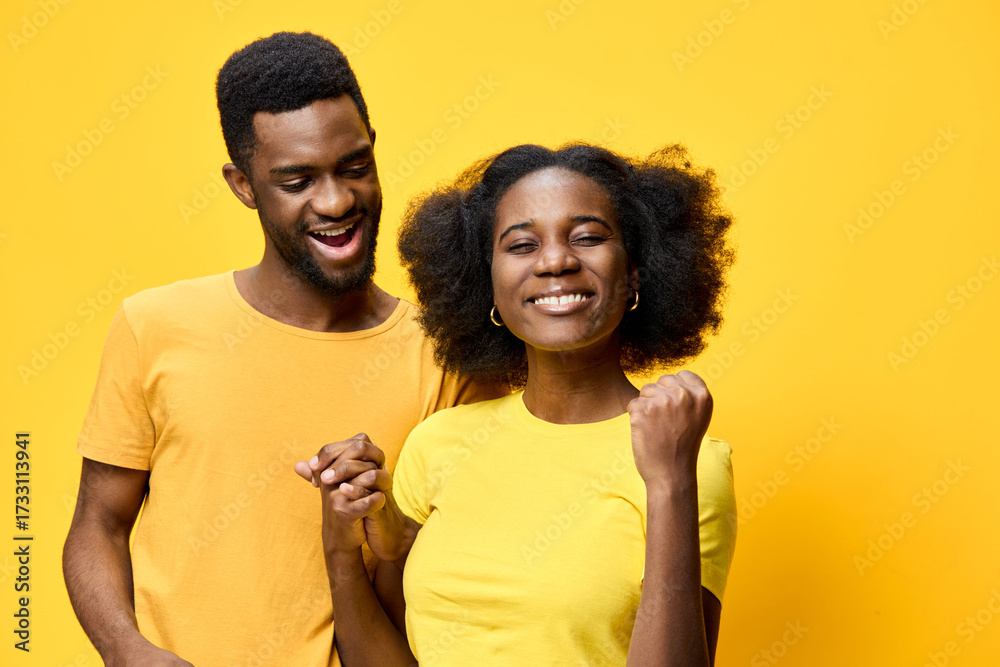 Fototapeta premium Happy young couple celebrating success in matching outfits against a vibrant yellow background, expressing joy and love
