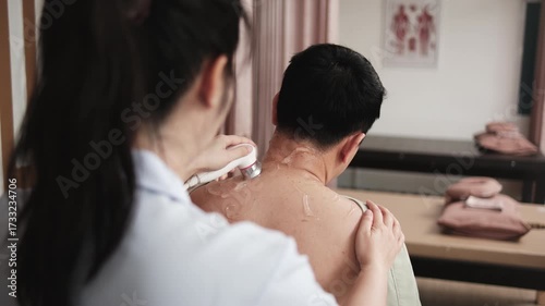 Male Asian patient is treated for healthy recovery, gel ultrasound for shoulder pain relief by female physical muscle doctor, passive medical therapy at spa clinic, and wellness massaging healthcare.