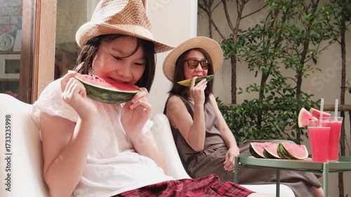 Chilling Asian family holidays, casual girl and mum enjoy eating pieces of fresh red watermelons sliced and smoothie drinks, happiness relaxing on vacation, and hot summertime at outdoor terrace.