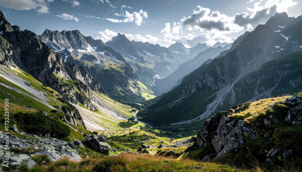 Fototapeta premium Dramatic Mountain Range Landscape with Green Valley and Sunlit Peaks Under Partly Cloudy Sky Wide Angle View