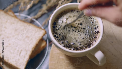 Top view of Person hand steering coffee in a cup with spoon. Breakfast morning of a cup hot black coffee on wooden background. footage b-roll Slow motion scene 4k. home making coffee.
