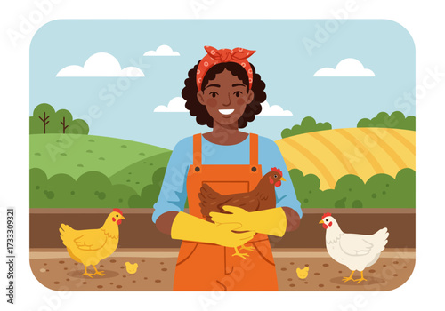 Happy African American woman farmer in overalls holding a chicken on a rural farm with other hens.