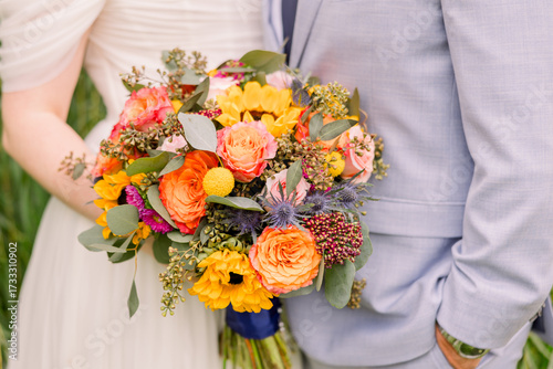 A bride and groom standing together and the bride holds a big wedding bouquet with orange and yellow and autumn colored flowers.