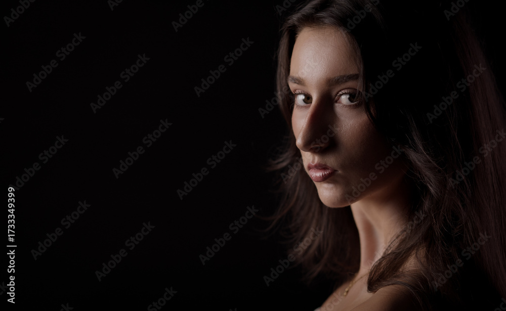 Naklejka premium Fashion model posing in studio with serious expression, looking over her shoulder against a dark background
