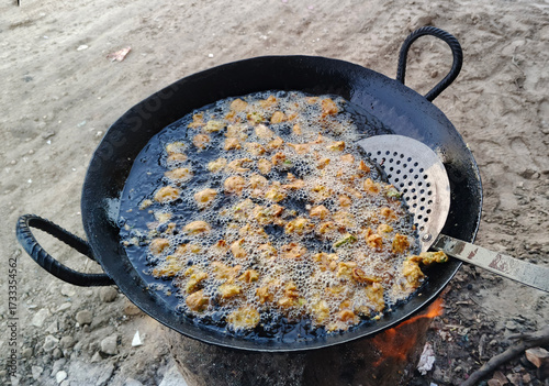 Crispy pakoras (fritters) being fried in a traditional pan. Freshly made and golden-brown, these tasty snacks are perfect for tea time or special occasions. This is a popular street food in India