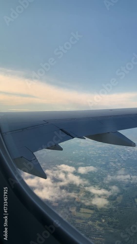 Vertical video. View from airplane window and wings next to the window. Airplane flying with a view of blue sky and fluffy white clouds from the airplane window.