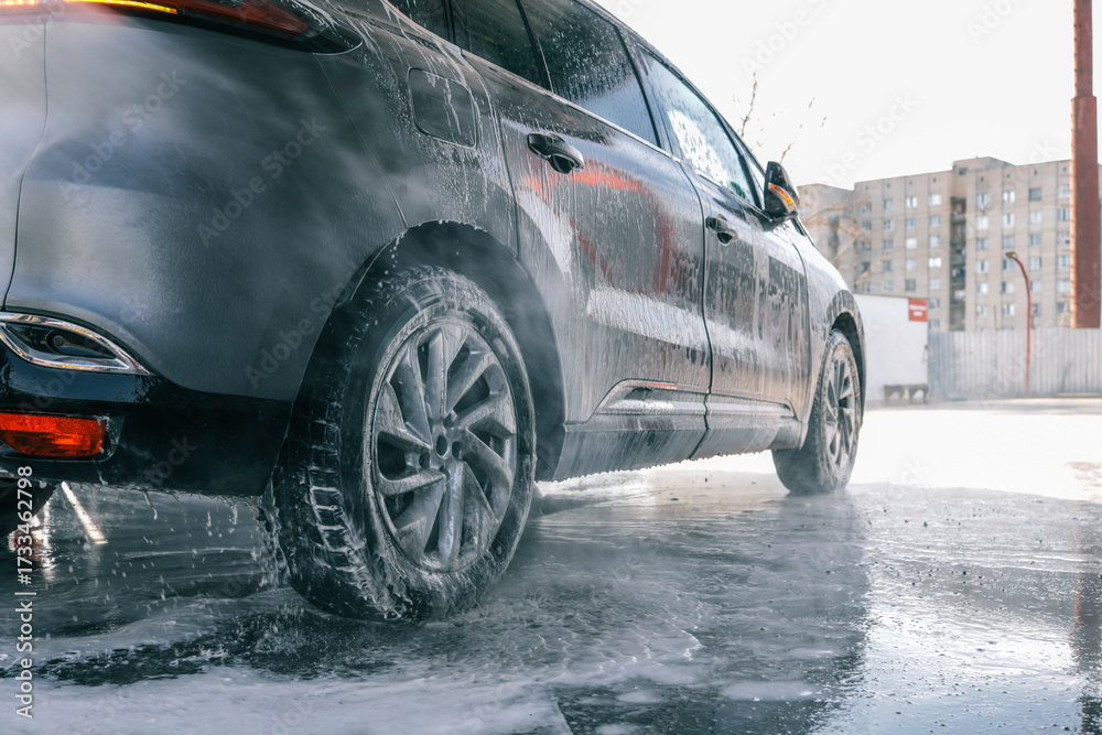 Naklejka premium Washing a dark car with soap and water at a car wash station.