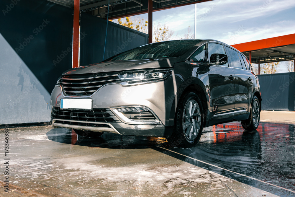 Obraz premium Shiny gray car being washed at a car wash station on a sunny day.