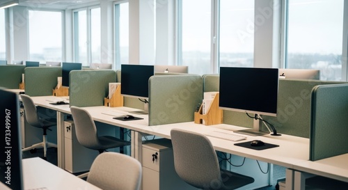 Rows of workstations fill a modern office space with large windows