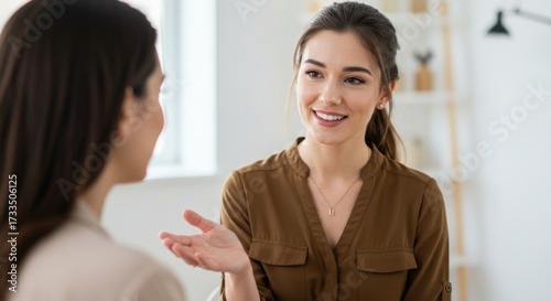 Two women engaged in a conversation. One is a young Asian woman with long brown hair, wearing a brown blouse. The other is a woman with dark hair, wearing a light top.