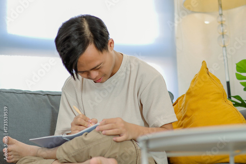 Teenager Boy with Down Syndrome Focused on Writing in His Journal in Cozy Living Room