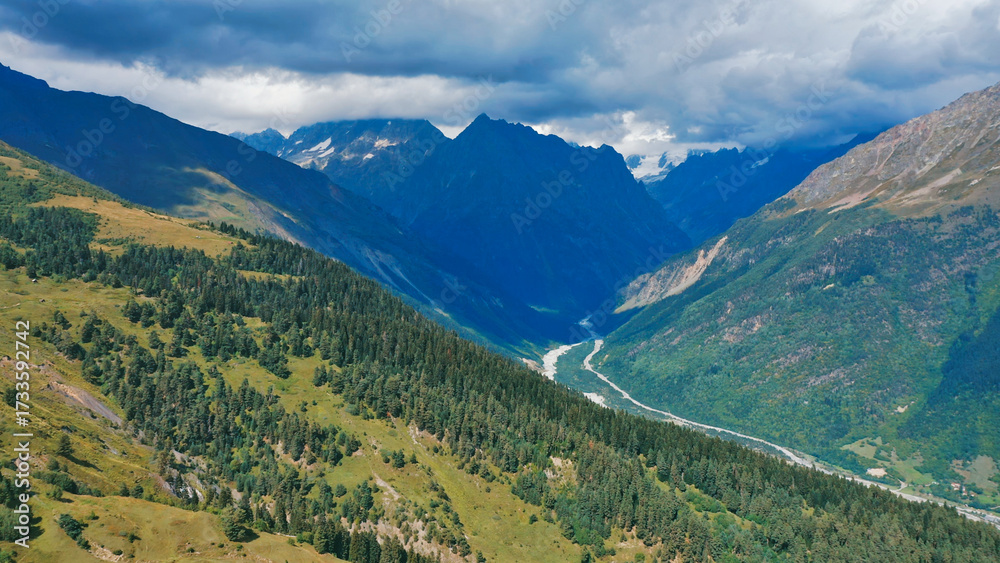 Fototapeta premium Aerial view of a mountain river flowing through a valley under snow-capped mountain peaks.